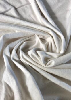 Close-up view of soft, knitted organic cotton jersey fabric showcasing its smooth texture and slightly off-white color.