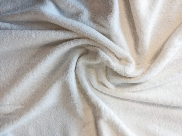 Close-up view of soft, thick organic cotton terry fabric showcasing its looped texture and unbleached ecru color.