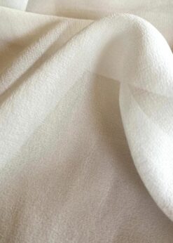 Close-up view of 100% mulberry silk georgette fabric with a slightly crinkled texture, soft drape, and a touch of transparency in a white color.